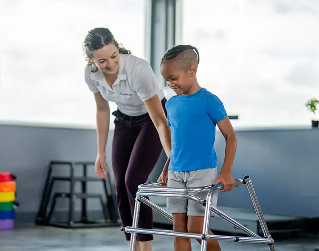 Boy with walker being helped by a physical therapist